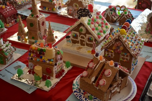 A colorful display of decorated gingerbread houses with various candies on a red tablecloth.