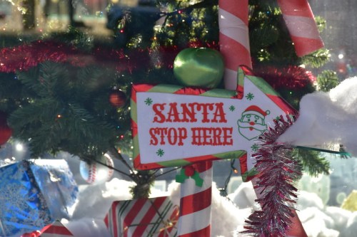 A festive sign reading "Santa Stop Here" with holiday decorations in the background.