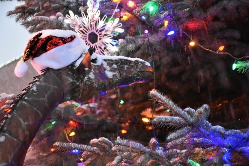 A decorated tree with colorful lights and a snow-covered giraffe wearing a Santa hat and a snowflake ornament.