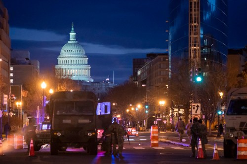 Nighttime view of the U.S. Capitol dome with military vehicles and traffic cones in the foreground.