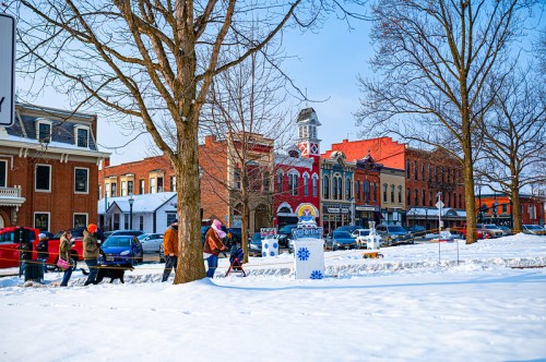 A snowy street scene with people walking, colorful buildings, and a clock tower in a small town.