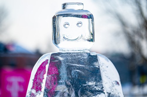 A clear ice sculpture of a smiling Lego-like figure against a snowy background.