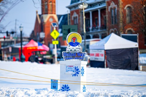 A United Way sign stands in a snowy area, with tents and a church visible in the background.