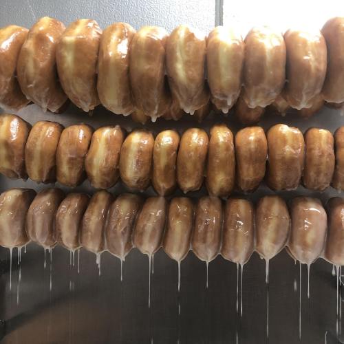A row of glazed donuts hanging, with glaze dripping down from each one.