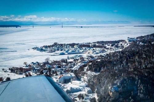 Aerial view of a snowy landscape with a small town and a bridge in the distance under a clear blue sky.