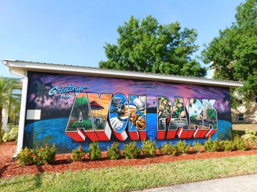 Colorful mural reading "Greetings from Avon Park" with vibrant designs and greenery in the background.