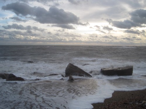 Waves crash against rocky shore under a cloudy sky, creating a serene coastal scene.