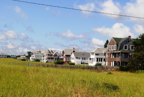 A row of charming houses along a grassy field under a blue sky with scattered clouds.
