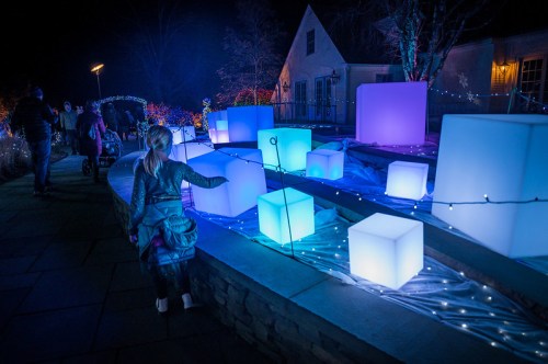 A child interacts with glowing, colorful cubes in a festive outdoor setting, surrounded by twinkling lights.