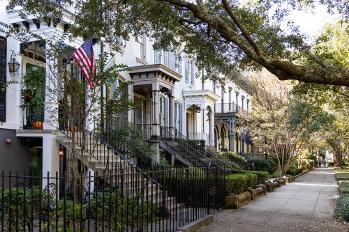 A tree-lined street featuring historic homes with porches, an American flag, and well-maintained gardens.