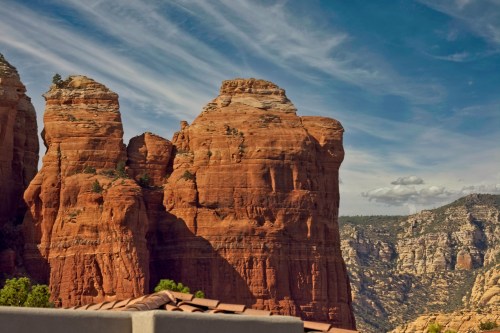 Red rock formations rise against a blue sky with wispy clouds, showcasing the natural beauty of the landscape.