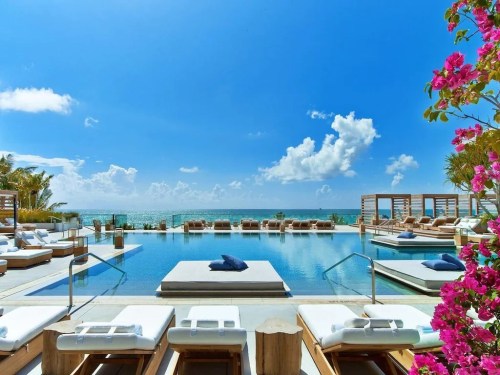 A luxurious poolside view with lounge chairs, vibrant flowers, and a clear blue sky overlooking the ocean.