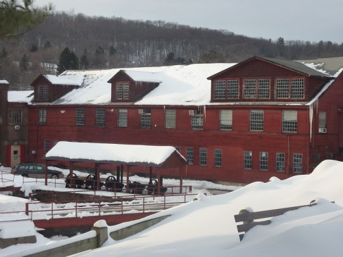 A red building with snow-covered roofs and a snowy landscape, surrounded by trees in a winter setting.