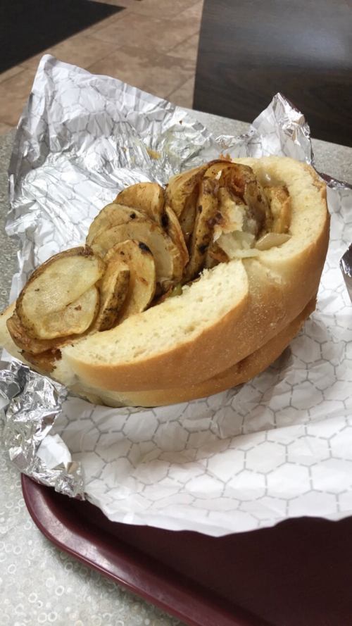 A sandwich filled with sliced, fried potatoes, served in a soft bun and wrapped in foil.