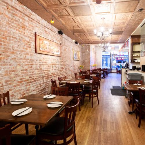 Cozy restaurant interior with wooden tables, chairs, and exposed brick walls, featuring warm lighting and a welcoming atmosphere.