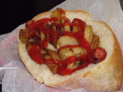 A bread roll filled with fried potatoes and sausage, topped with ketchup.
