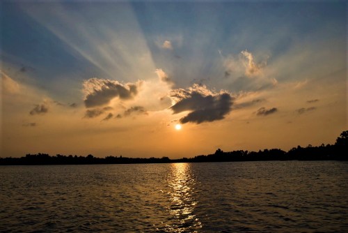 A serene sunset over a calm lake, with rays of light breaking through clouds and reflecting on the water.