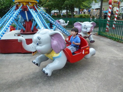 A child rides a colorful elephant carousel at an amusement park, smiling as the elephants spin around.