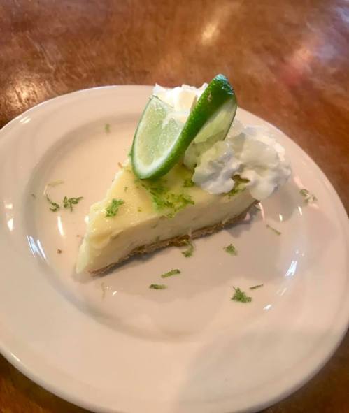 A slice of key lime pie topped with whipped cream and a lime wedge, served on a white plate.