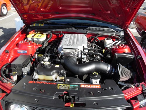 Close-up of a red car's engine bay, showcasing the engine, air intake, and various components under the hood.