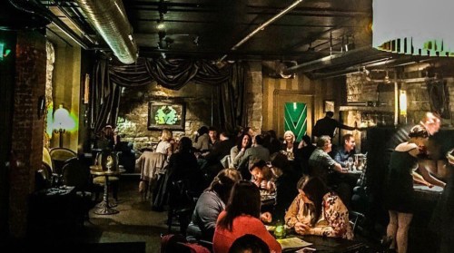 A dimly lit restaurant with patrons dining at tables, featuring exposed brick walls and stylish decor.