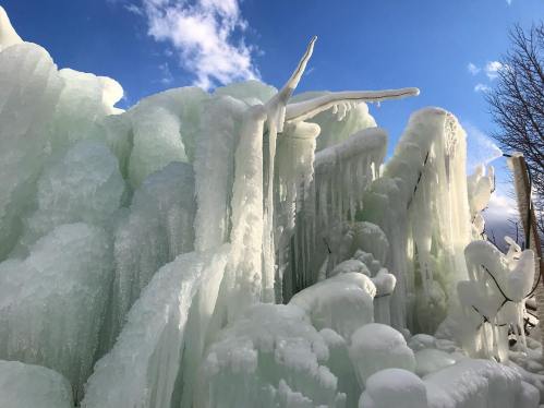 A stunning formation of ice and icicles against a bright blue sky with scattered clouds.