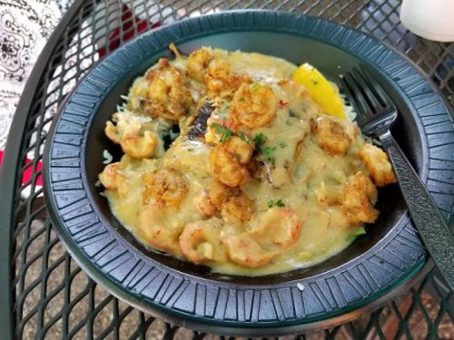A plate of shrimp and grits topped with fried shrimp, served with a lemon wedge on a black plate.