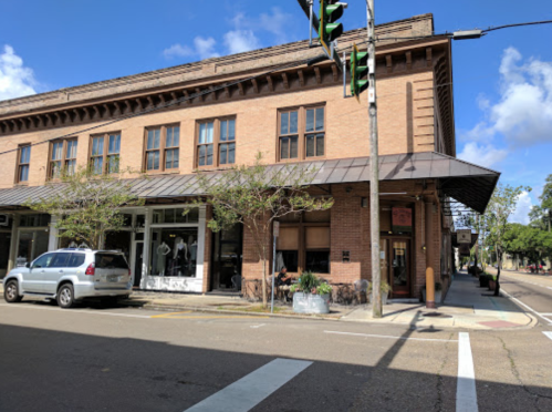 A brick building with large windows, featuring shops on the ground floor and a traffic light in the foreground.