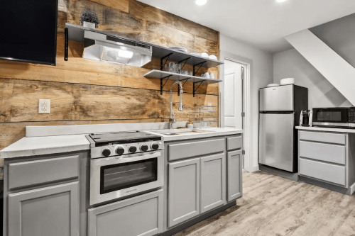 Modern kitchen with gray cabinets, wooden accent wall, stainless steel appliances, and open shelving.