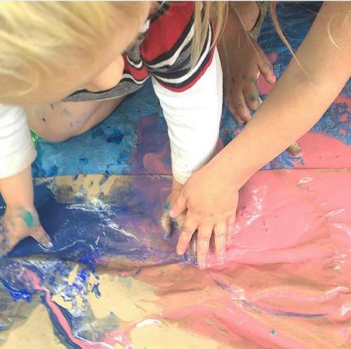 Two children with paint-covered hands are playing on a colorful surface, creating art together.
