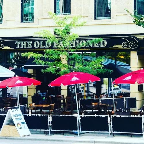 Exterior of a restaurant called "The Old Fashioned," featuring red umbrellas and outdoor seating.