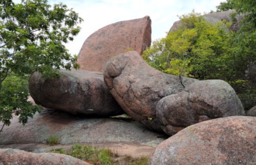 Two large, weathered boulders are positioned among green foliage, set against a cloudy sky.
