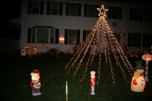 A festive yard display with a lit Christmas tree, colorful decorations, and cheerful holiday figures.