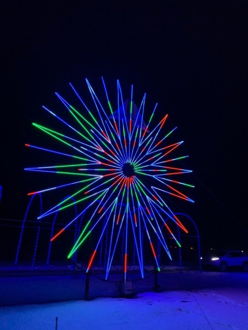 A colorful light display in a starburst pattern, featuring blue, green, and red lights against a dark night sky.