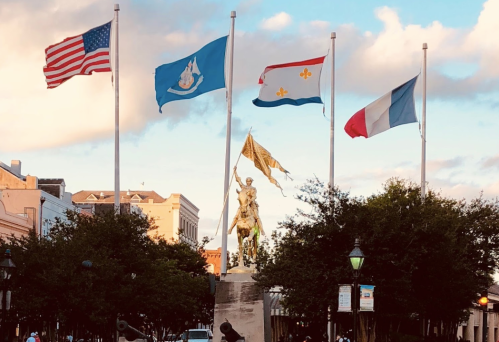 A statue stands in a park, surrounded by flags, including the American flag and state flags, against a cloudy sky.