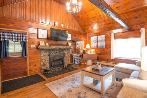 Cozy wooden living room with a stone fireplace, TV, and comfortable seating, featuring warm lighting and rustic decor.