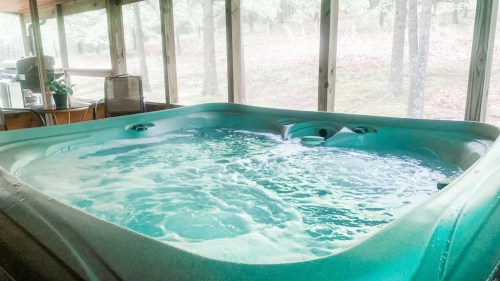 A bubbling hot tub indoors, surrounded by large windows with a view of a forested area.