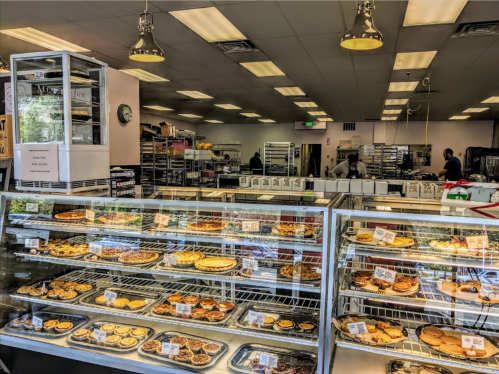 A bakery display case filled with various pastries and desserts, with bakers working in the background.