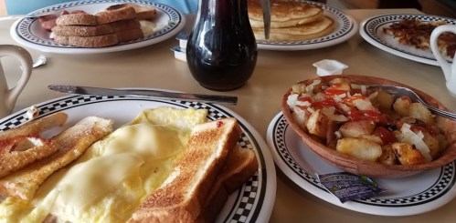 A breakfast spread featuring eggs, toast, pancakes, and a bowl of potatoes with toppings on a table.
