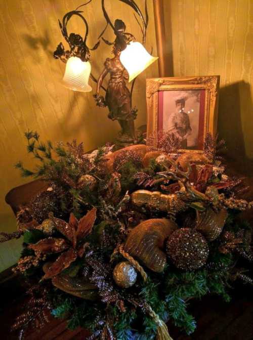 A decorative arrangement with pine, ornaments, and a vintage photo in a framed portrait beside a lamp.