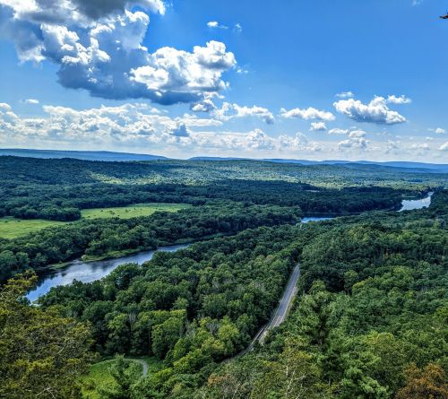 A scenic view of lush green hills and a winding river under a bright blue sky with fluffy clouds.