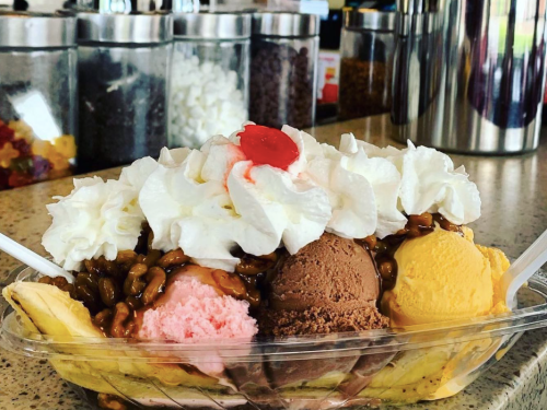 A colorful banana split topped with whipped cream, a cherry, and chocolate sauce, served in a clear dish.