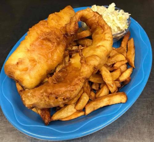 A blue plate with two pieces of fried fish, golden fries, and a small bowl of coleslaw.