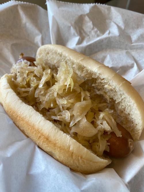 A hot dog in a bun topped with sauerkraut, served in white paper.