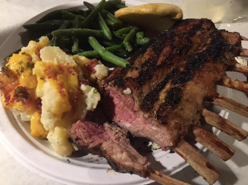 A plate featuring grilled rib rack, green beans, and cheesy mashed potatoes, with a slice of bread on the side.