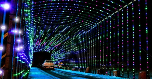 A brightly lit tunnel adorned with colorful lights in green, blue, and pink, with a car driving through.
