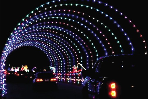 A colorful light tunnel with vibrant, multicolored lights illuminating a dark night, with cars driving through.