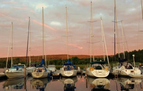 Sailboats docked in a marina at sunset, reflecting on calm water with a colorful sky in the background.