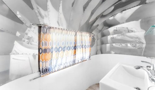 Interior of a modern bathroom with shiny metallic walls, a colorful curtain, and a sleek sink.