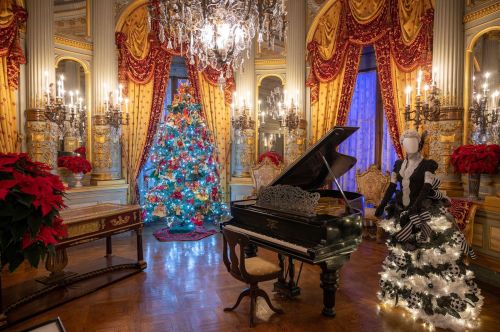 A festive room with a grand piano, a decorated Christmas tree, and a mannequin in a black and white dress, surrounded by holiday decor.